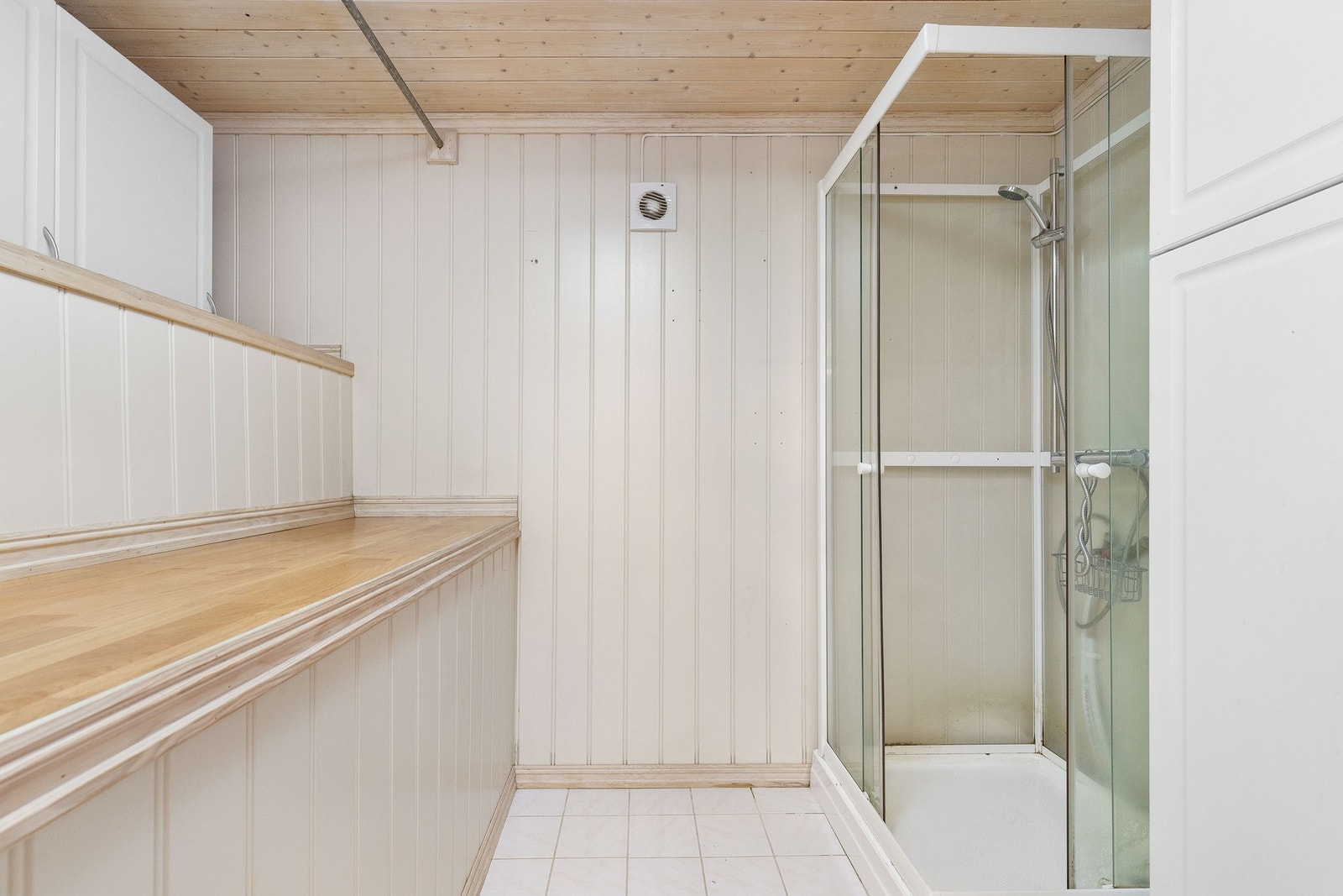 Lyst baderom med dusjkabinett, flislagt gulv og panelvegger. Galleribilde