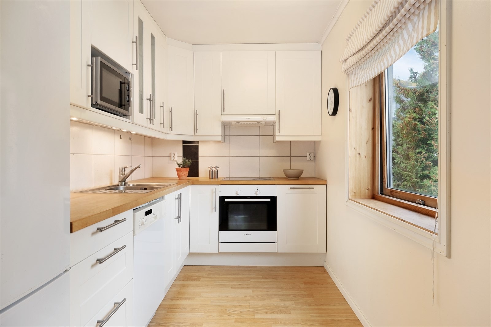 Kjøkkenet har innreiing med glatte frontar og benkeplate av heiltre. Her er det kvitevarer som kjøl/fryseskap, oppvaskmaskin, platetopp og steikeovn. Galleribilde