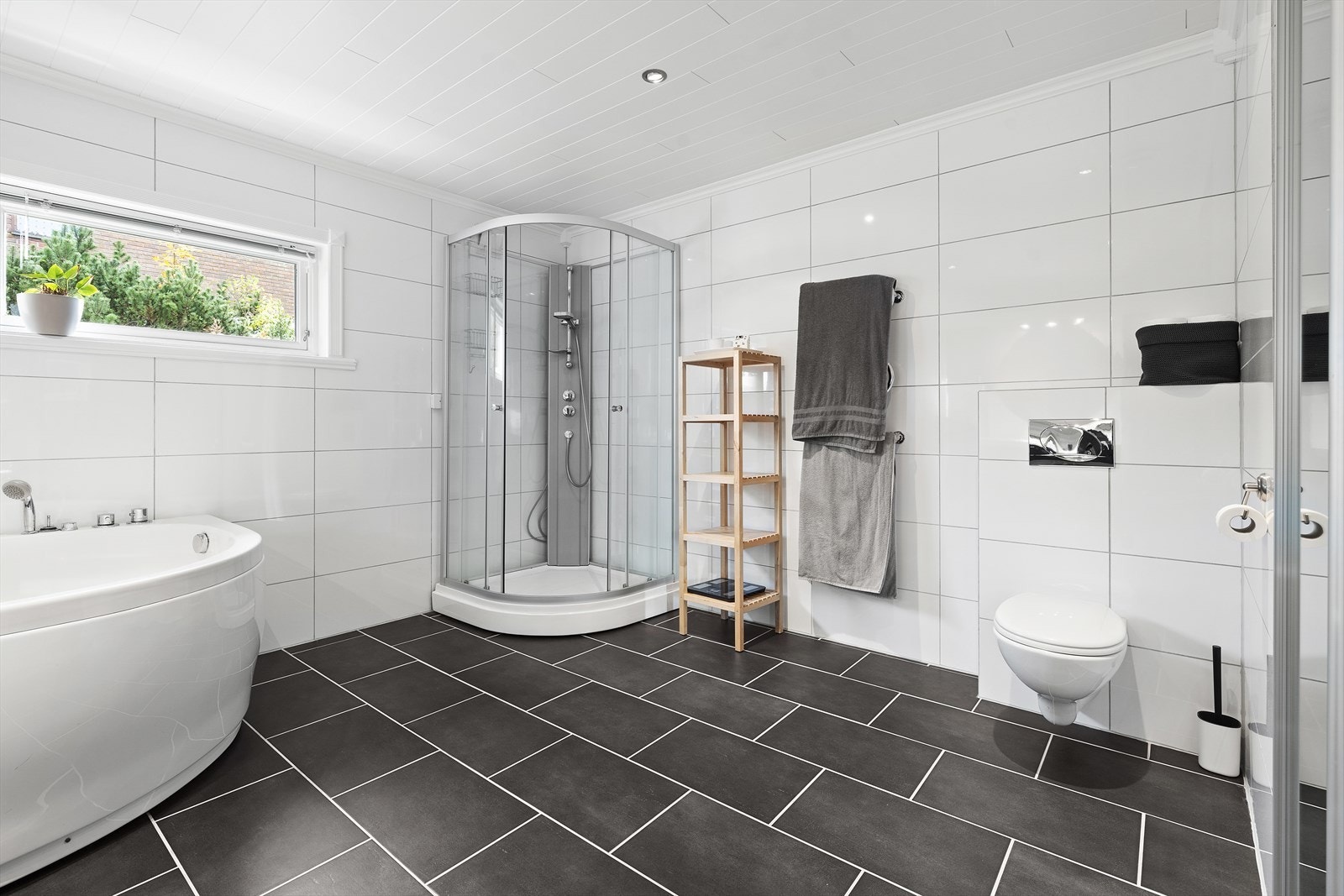 Baderommet er utstyrt med servant over skuffeinnredning, speil med overliggende belysning, vegghengt skap, vegghengt toalett, badekar og dusjkabinett. I tillegg er det en romslig skyvedørsgarderobe med speilfronter Galleribilde