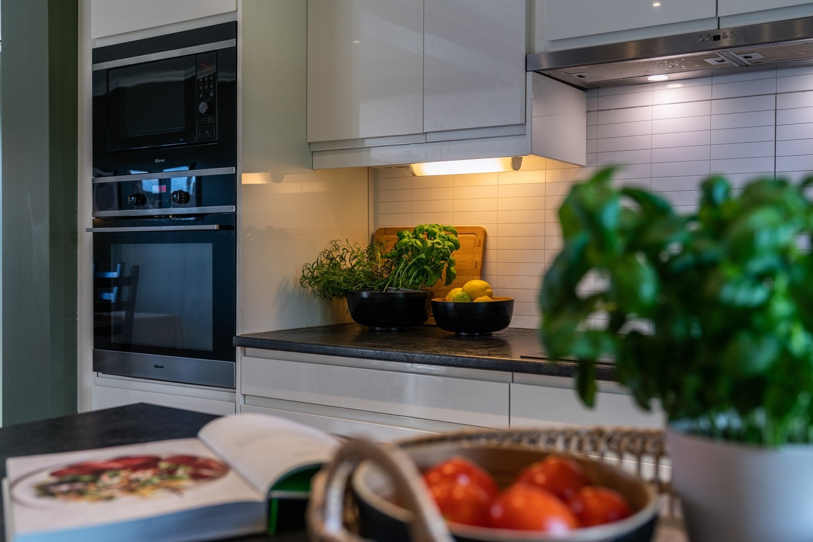 Vannfaste plater over benkeplate av laminat, med nedfelt induksjonstopp og benkebeslag i kompositt. Ventilator over kokesonen. Galleribilde