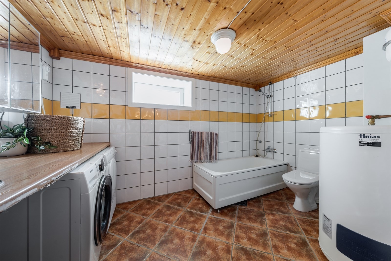 Bad/vaskerom er flislagt og har toalett, badekar, varmtvannstank og benkeplate av laminat med nedfelt stålkum, samt opplegg for vaskemaskin og tørketrommel. Galleribilde