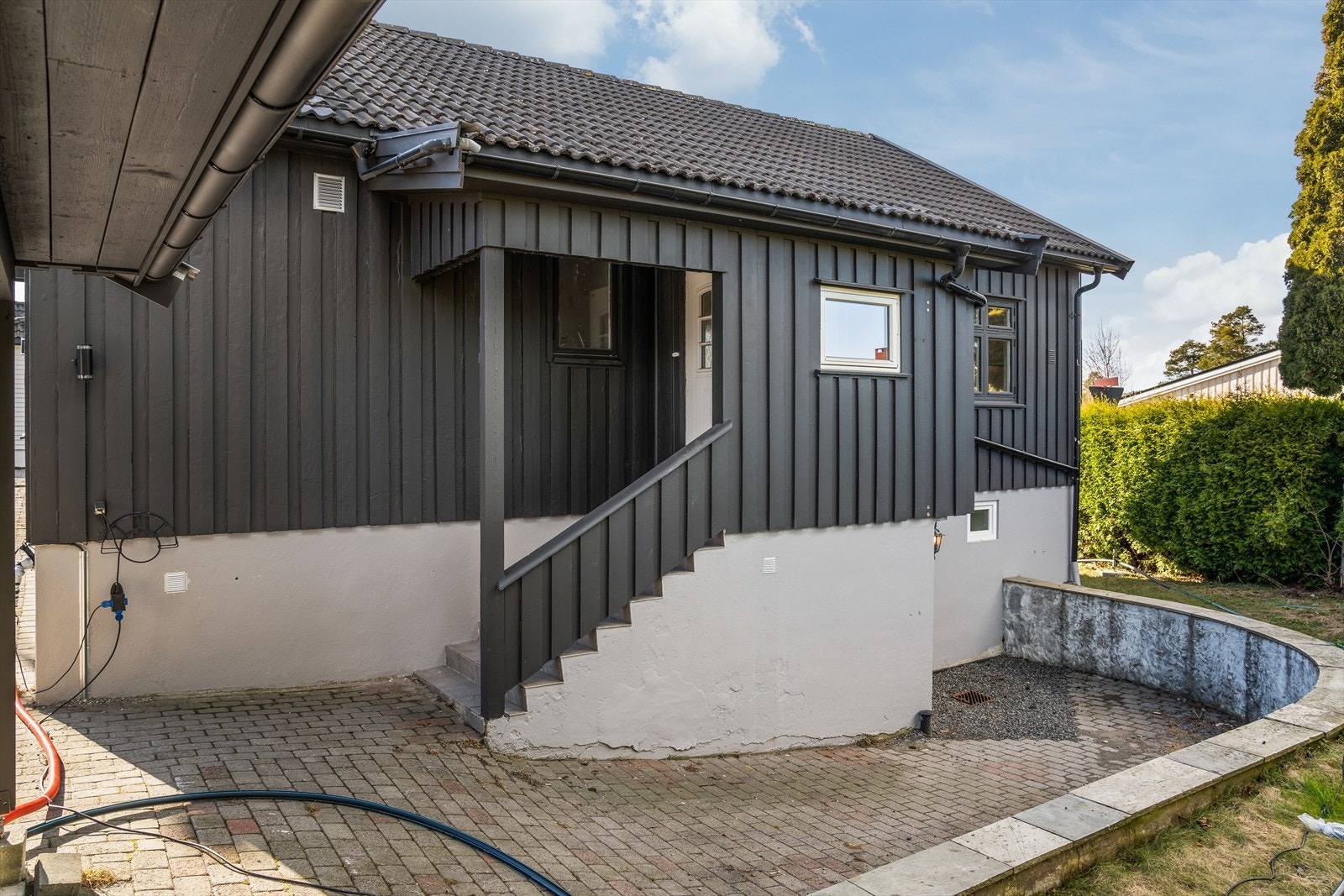Støpt betongtrapp med flis og rekkverk til overbygget inngangsparti. Boligen har også kjellerinngang, med kjellerdør i malt tre. Galleribilde