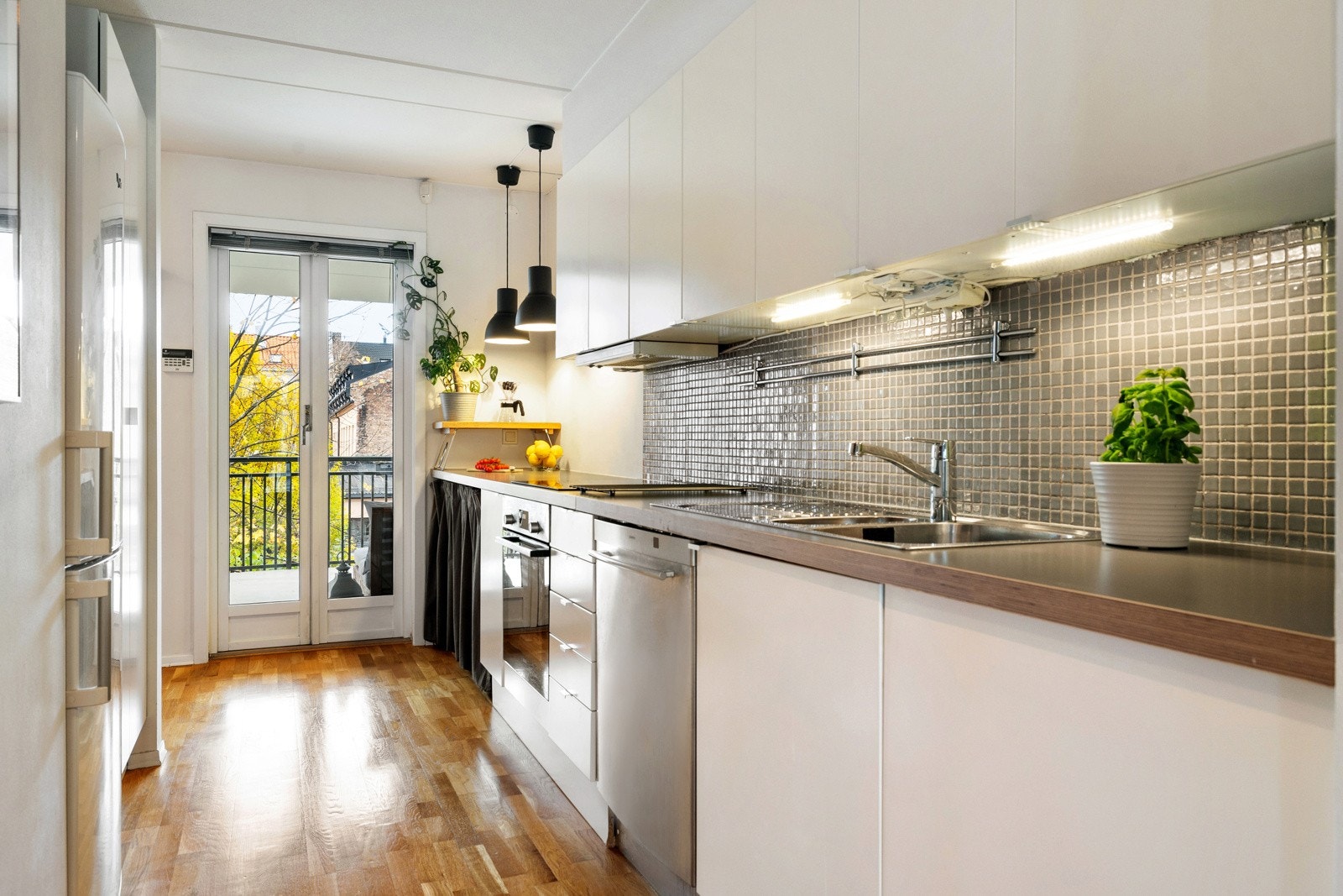 Kjøkkenet er lyst og funksjonelt med hvit innredning, grå laminatbenkeplate og mosaikkfliser mellom benk og overskap. LED-belysning og stikkontakter under overskap gir både godt arbeidslys. Galleribilde