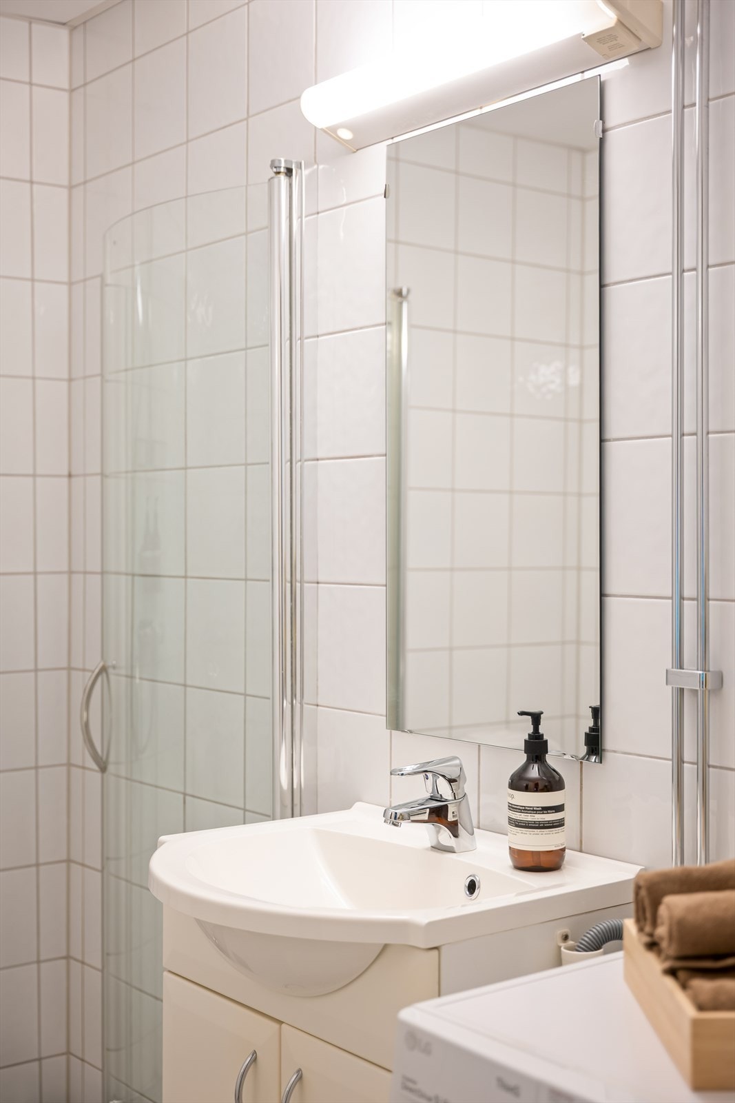 Her finner du en praktisk baderomsinnredning med servant og underskap, speil med overlys, dusjhjørne og et gulvmontert toalett. Galleribilde