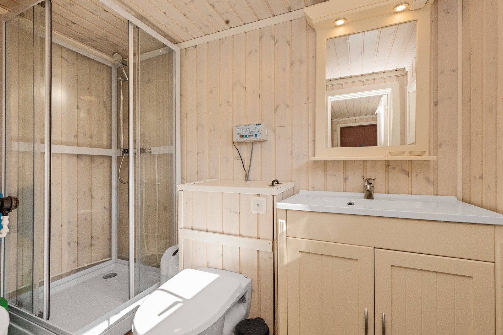 Badet har innredning med underskap og nedfelt servant i benk, jets toalett og dusjkabinett med sisterne for vann Galleribilde