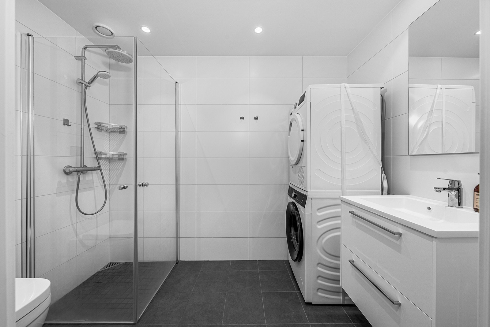 Videre er badet utstyrt med dusjhjørne med svingbare dusjdører i herdet glass. Det er også tilrettelagt for vaskemaskin og tørketrommel, som gir en praktisk løsning for klesvask Galleribilde