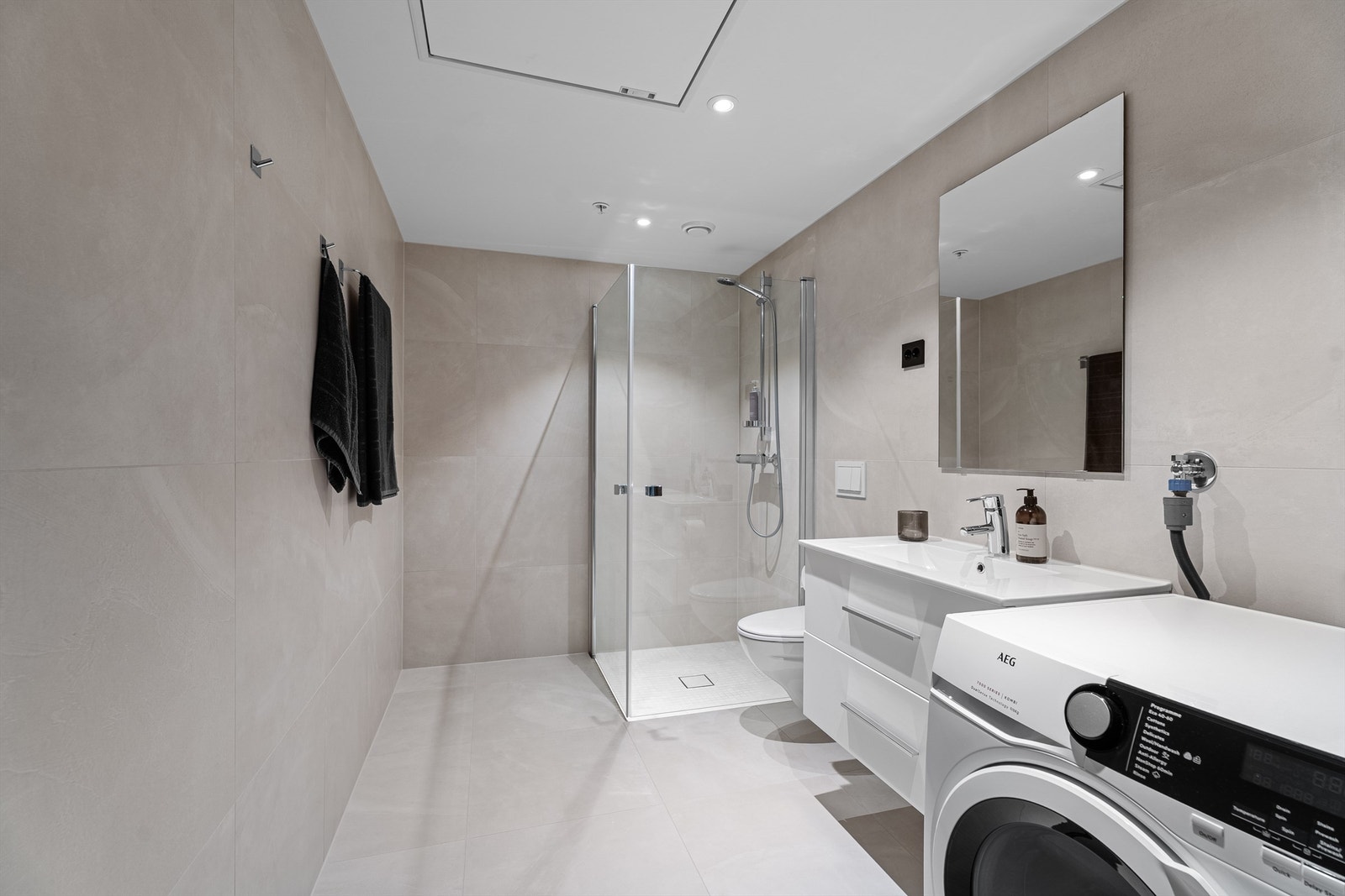 Lekkert flislagt bad med vegghengt toalett, dusjnisje med innfellbare dører samt servant med oppbevaring. Galleribilde