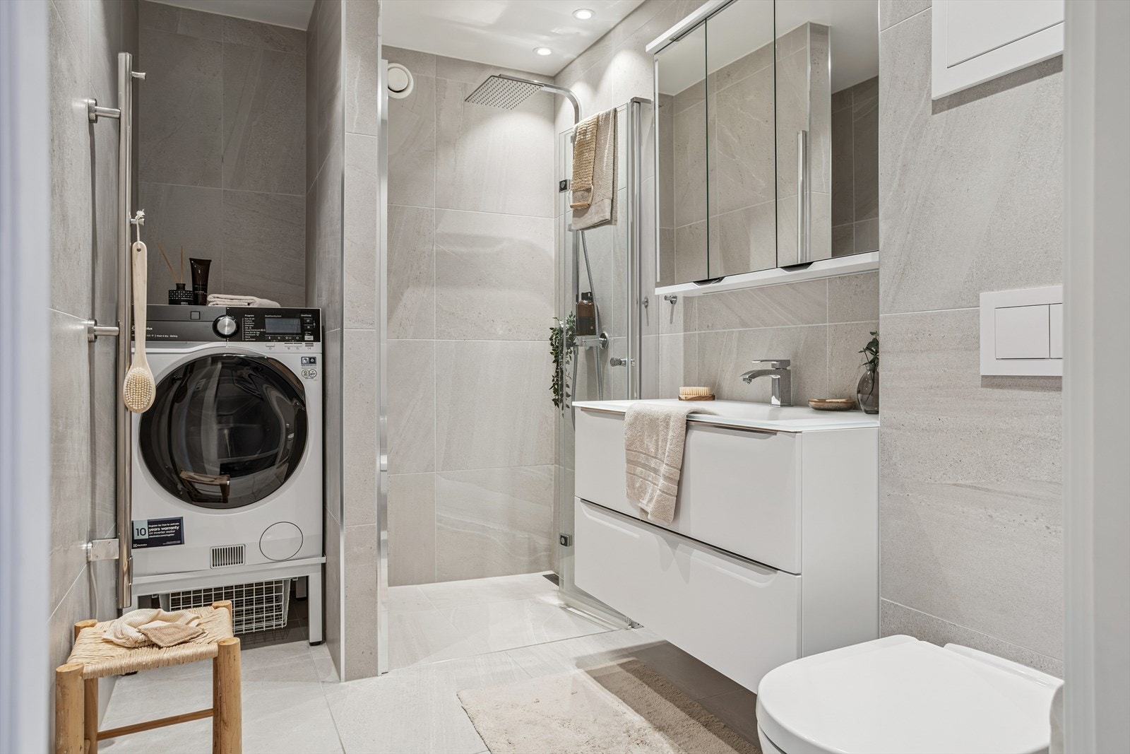 Lekkert og delikat bad fra 2021. Badet inneholder vegghengt toalett, dusj med glass foldedør, servant med møblement, speil og belysning. Det er elektriske varmekabler i gulv. Det er opplegg for vaskemaskin Galleribilde