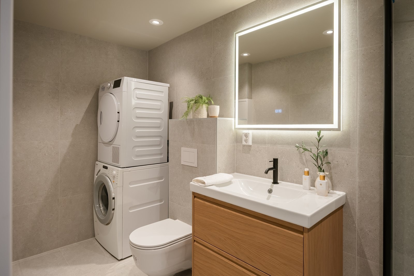 Badet har flislagte vegger- og gulv, opplegg for vaskemaskin, servant med underskap, varmekabler i gulv og dusj. Galleribilde