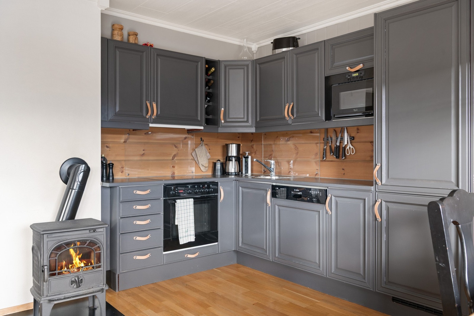 Kjøkken med integrerte hvitevarer, stilrene fronter og praktiske løsninger, med peisovn som gir en lun og hyggelig atmosfære Galleribilde