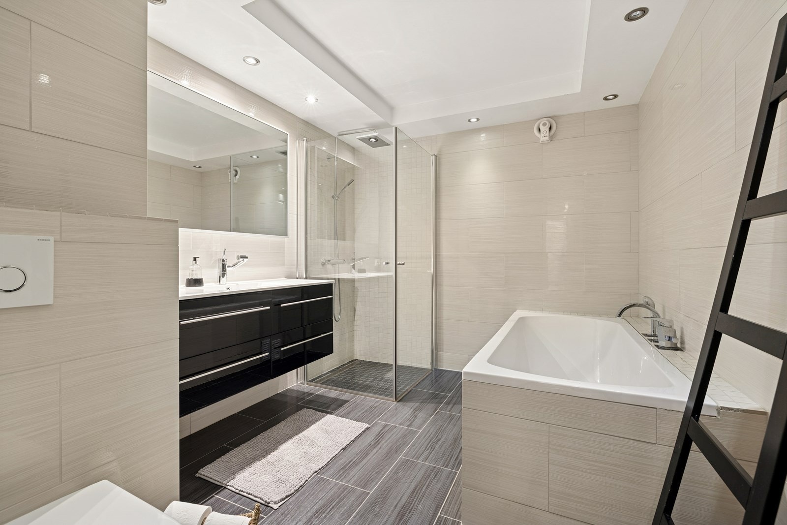 Badet fremstår moderne og stilrent, med dusjhjørne, flislagt badekar og vegghengt toalett. Galleribilde