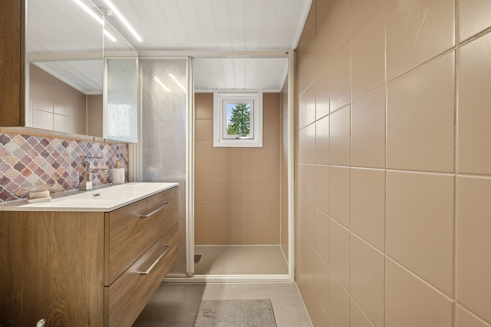 Badet i 2. etasje har fliser på veggene og vinylfliser på gulvet. Innredet med dusj, servant med skap, speil og toalett. Galleribilde