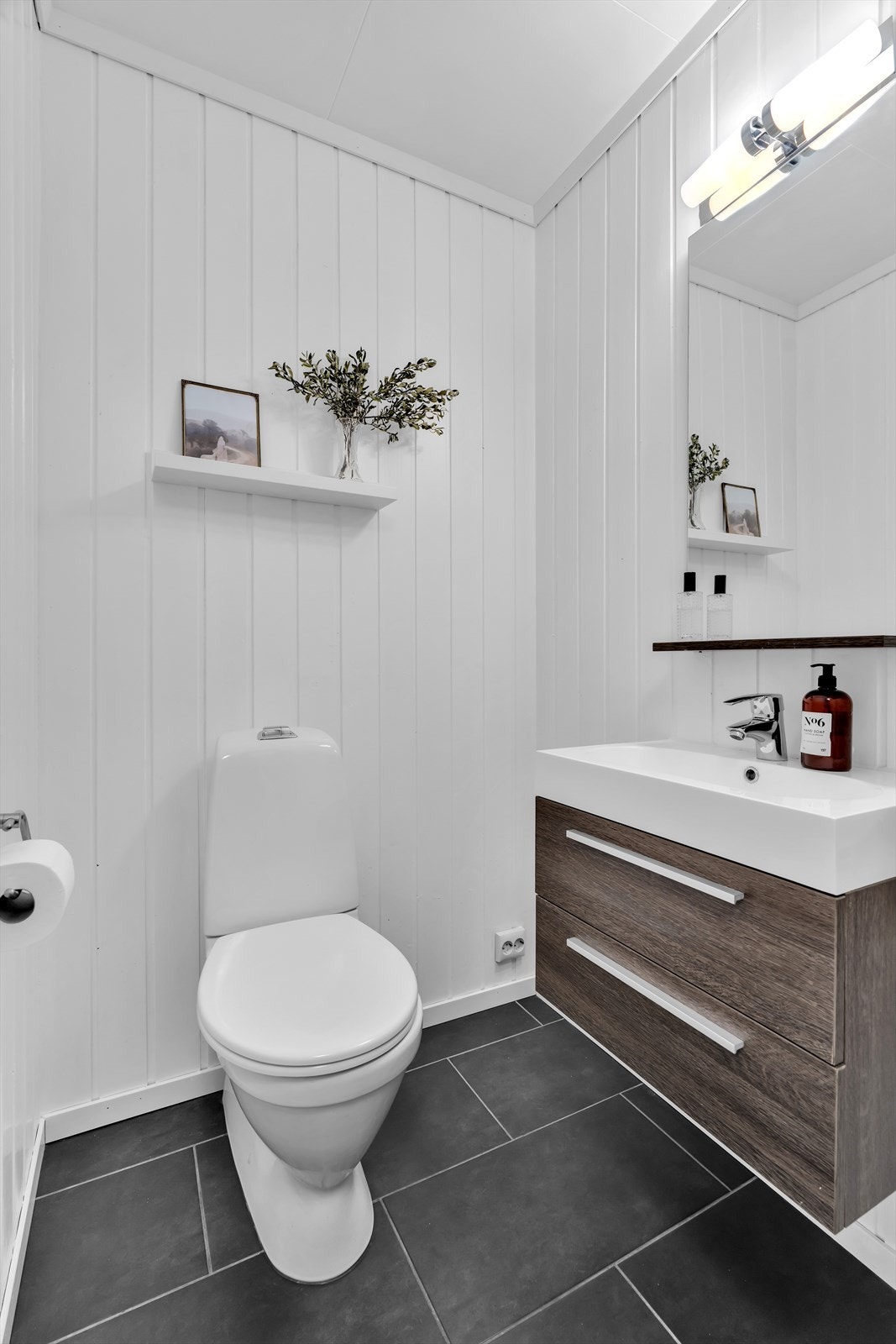 Toalettrommet har flislagt gulv og en moderne innredning med praktiske skuffer. Det inneholder vegghengt toalett samt et speil med integrert belysning over, som gir et stilrent preg. Galleribilde