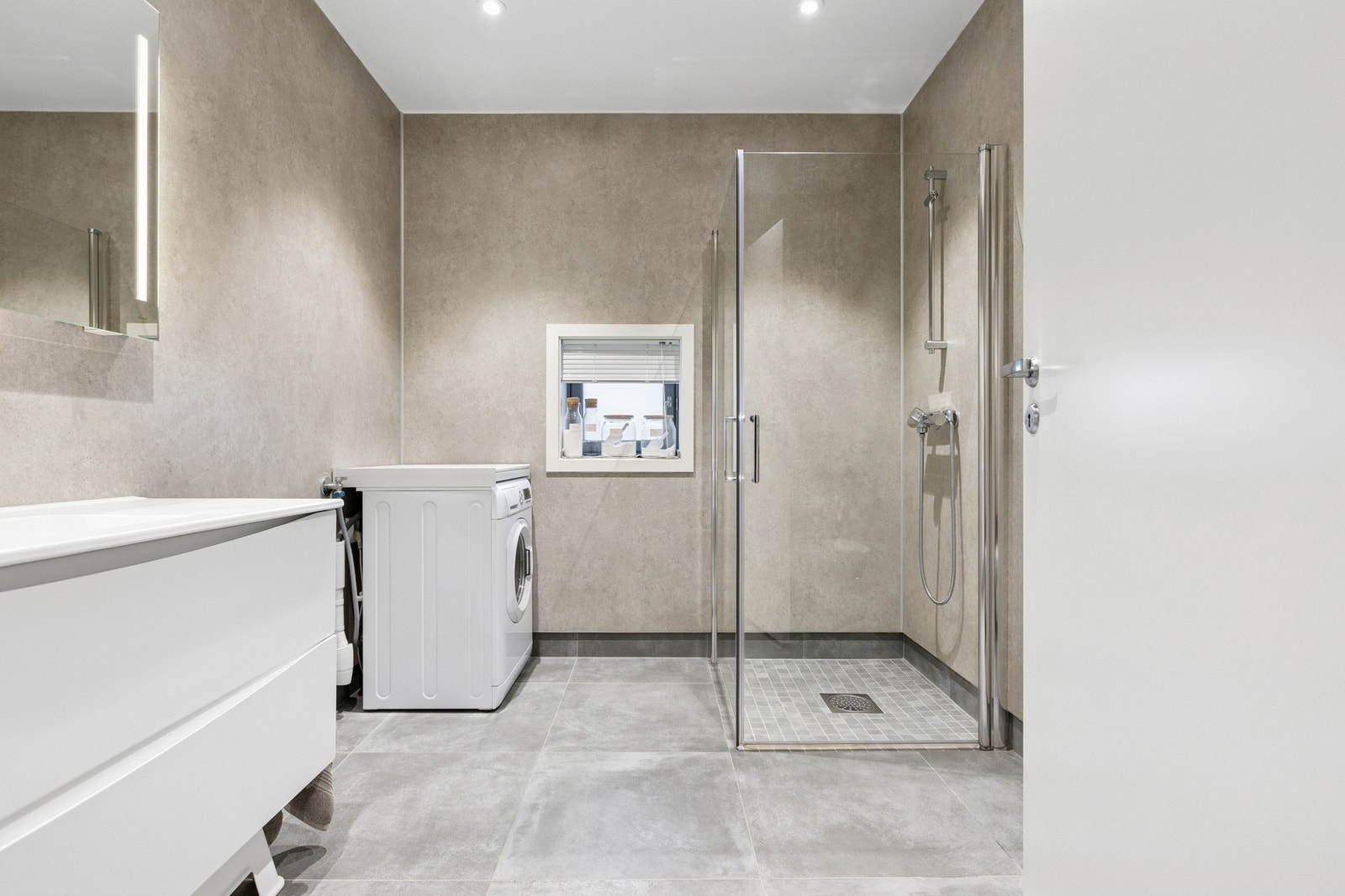 Dette er et delikat bad med vegghengt toalett, opplegg for vaskemaskin og downlights i himling. Galleribilde