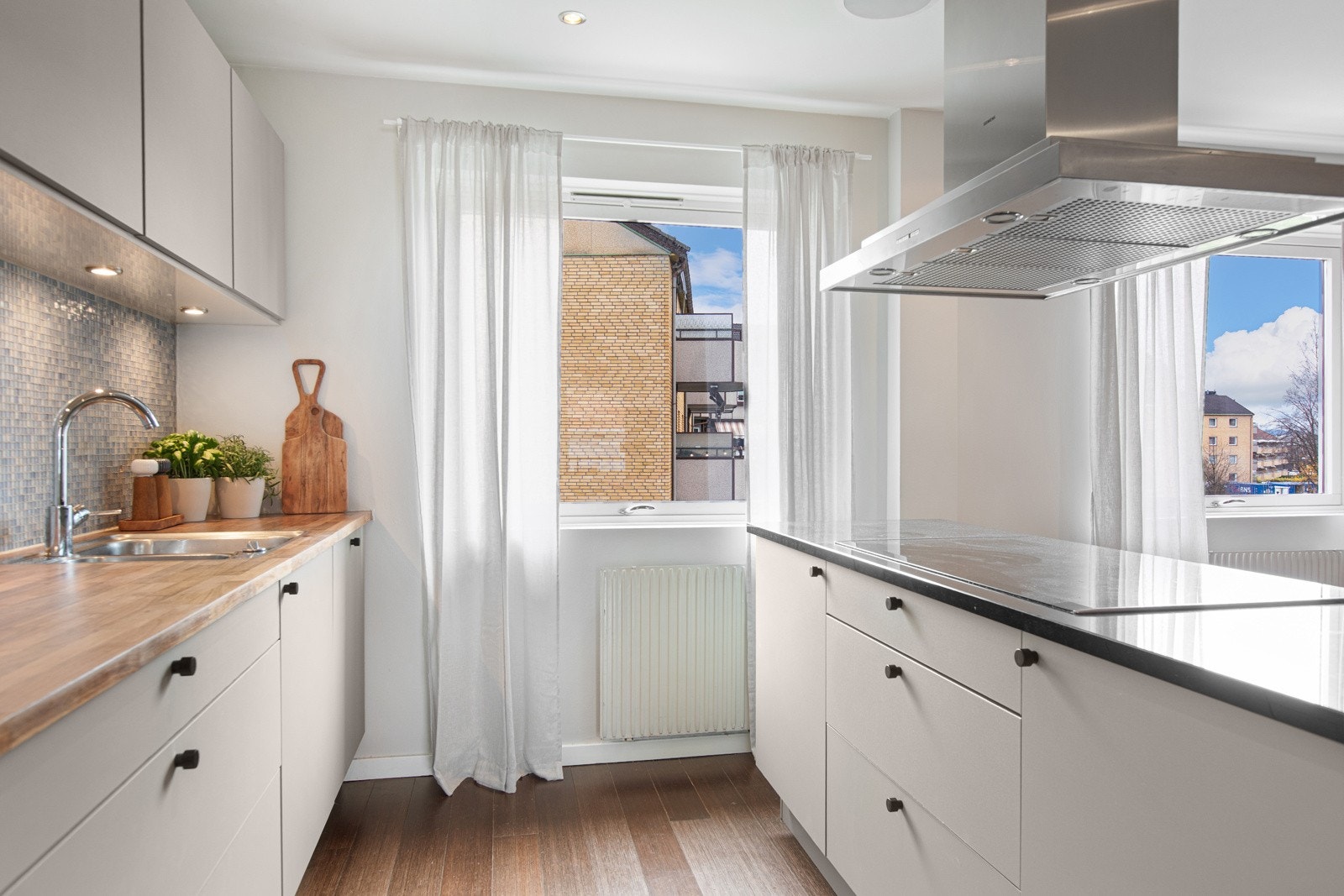 Kjøkkenet har en moderne innredning med glatte fronter, mosaikkfliser på vegg og kombinert benkeplate av stein og laminat. Galleribilde