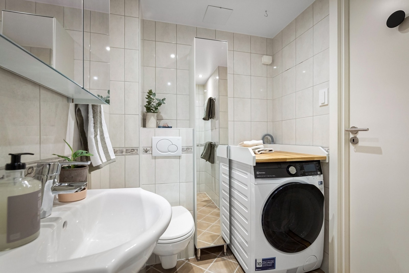 Badet er utstyrt med vegghengt toalett, dusjhjørne med innfellbar glassdører, heldekkende servant med skapinnredning under og speilskap på vegg. Galleribilde