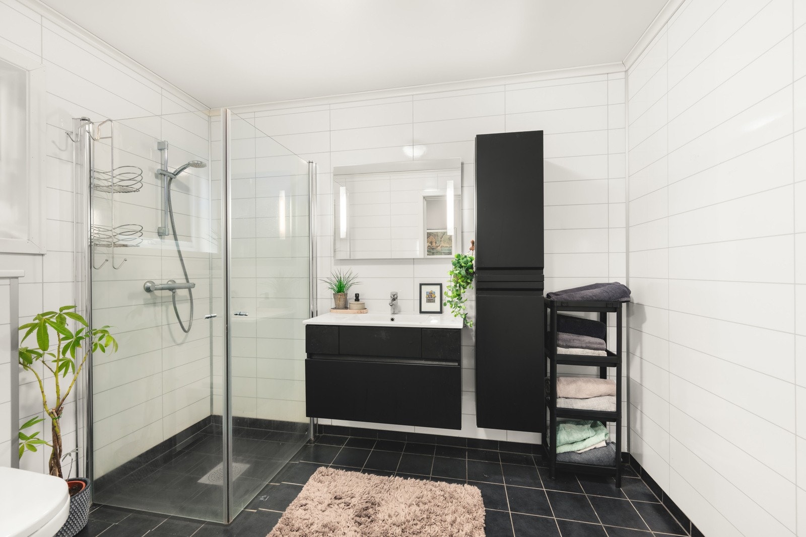 Smakfullt bad med flislagt gulv med varme og fliser på vegger. Badet har moderne innredning med servant og oppbevaringsplass, vegghengt toalett og dusjhjørne med glassvegg. Et elegant og praktisk baderom med tidløs standard. Galleribilde