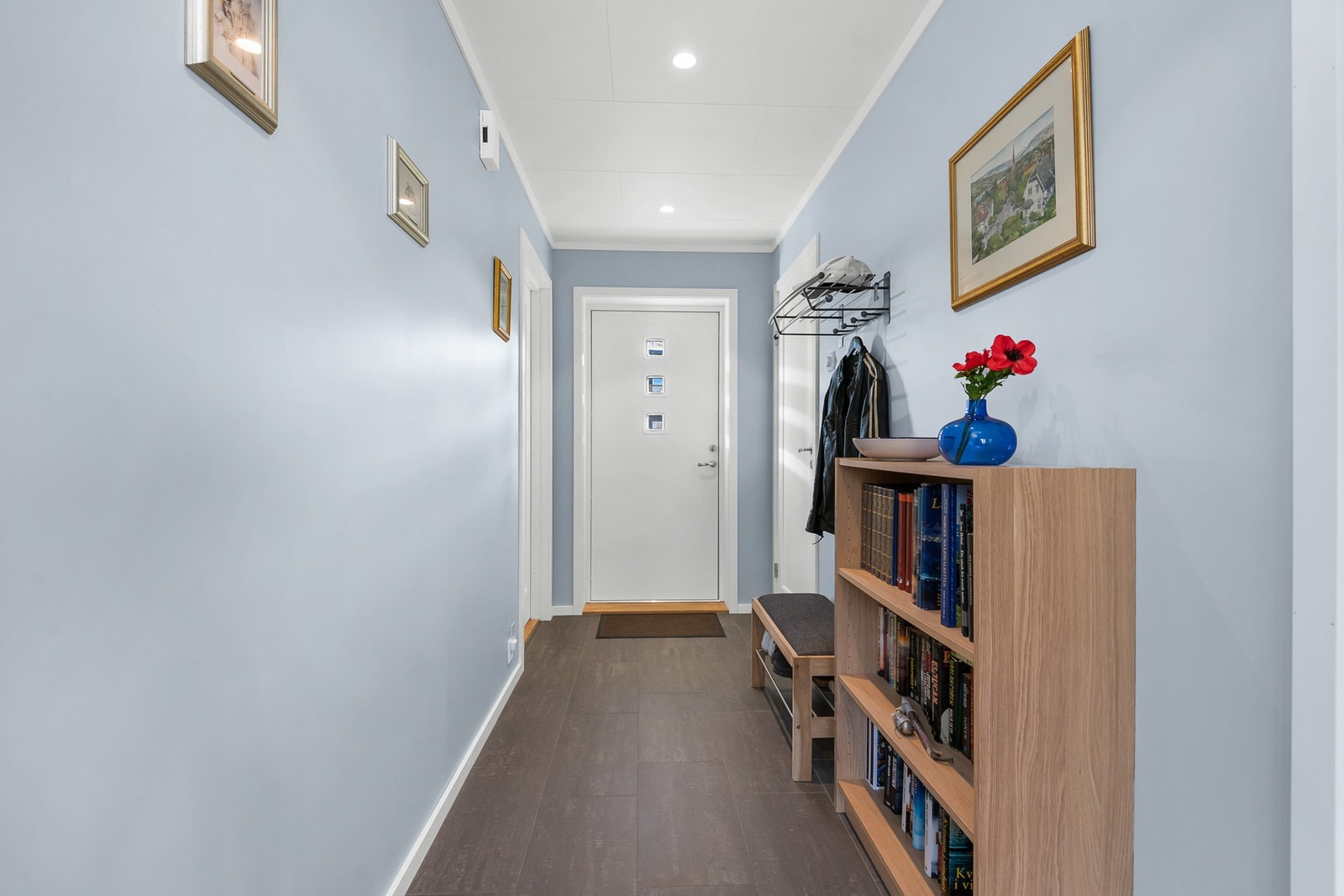 Gangen er lys med malte vegger i en dempet blågrå tone og mørkt, slitesterke fliser i starten av gangen som senere går over i parkett. Galleribilde