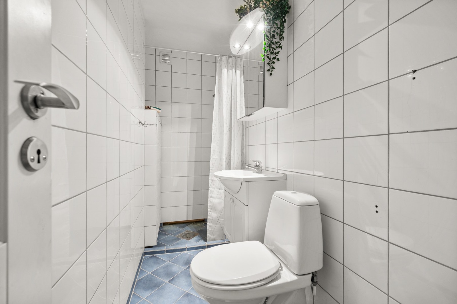 Det andre badet er flislagt og har en varmtvannsbereder som avgir varme til rommet. Her finner du servantseksjon med skap, dusjnisje med forheng, gulvmontert toalett samt overskap med speilfronter og lys. Galleribilde