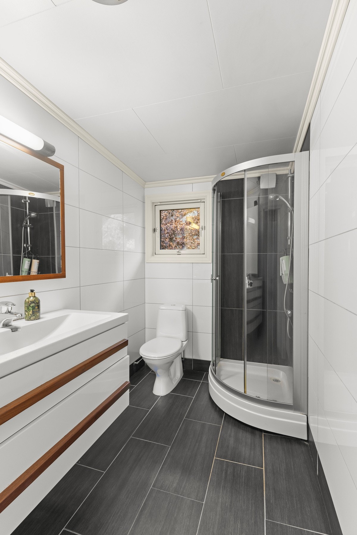 Pent bad med fliser på gulv og vegger, moderne innredning, speil, dusjkabinett og varme i gulvet. Galleribilde