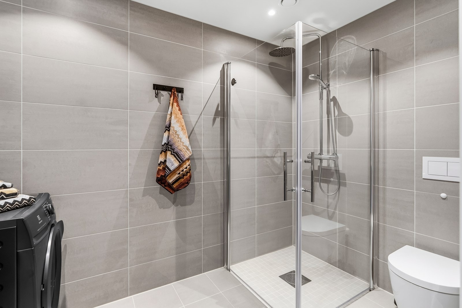 Badet har dusj på gulv med dører i herdet glass, veggfestet klosett og servant med underskap. I tillegg har badet opplegg for vaskemaskin. Galleribilde