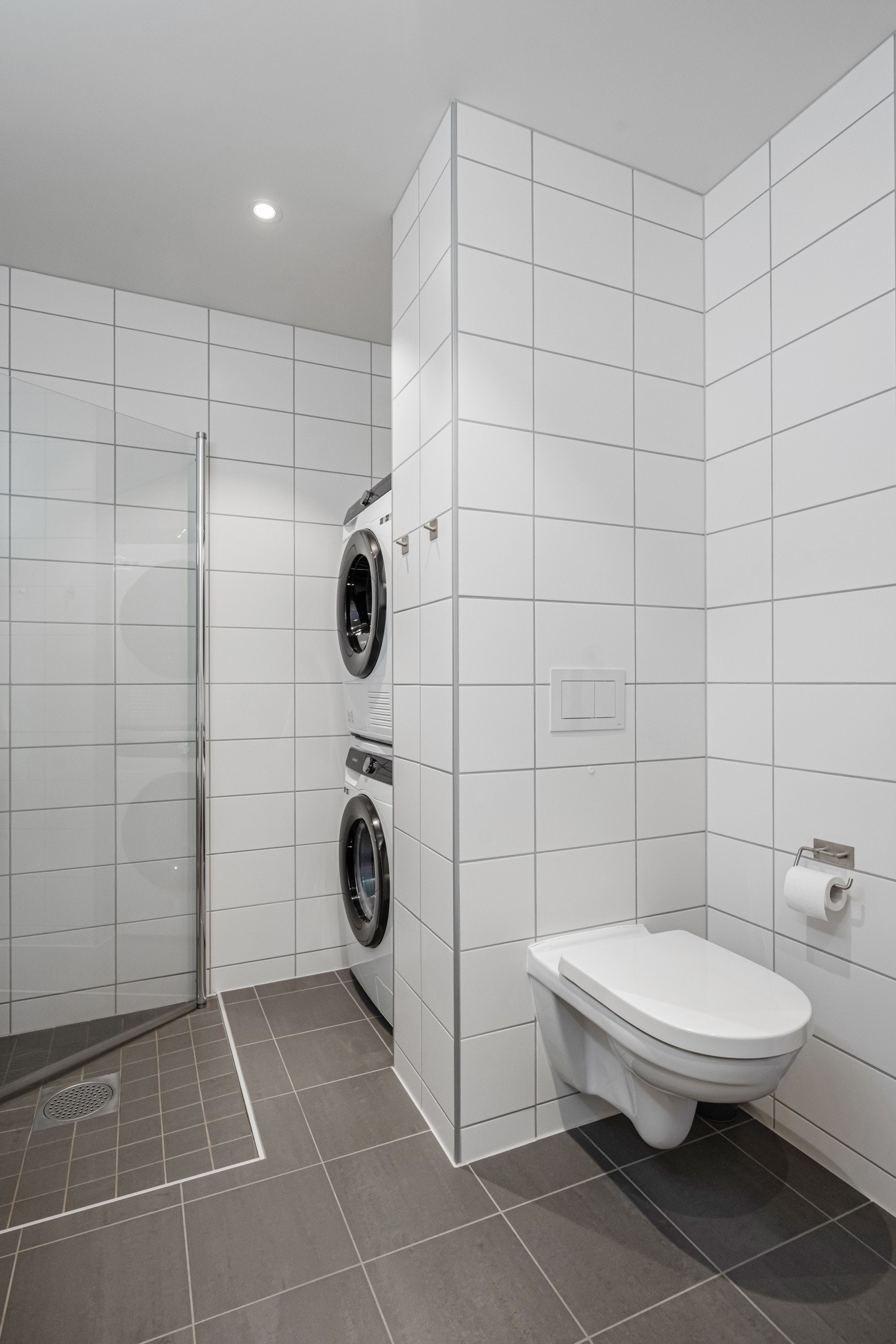 Rommet er innredet med baderomsinnredning, vegghengt wc, dusj og plass for vaskemaskin og tørketrommel. Galleribilde