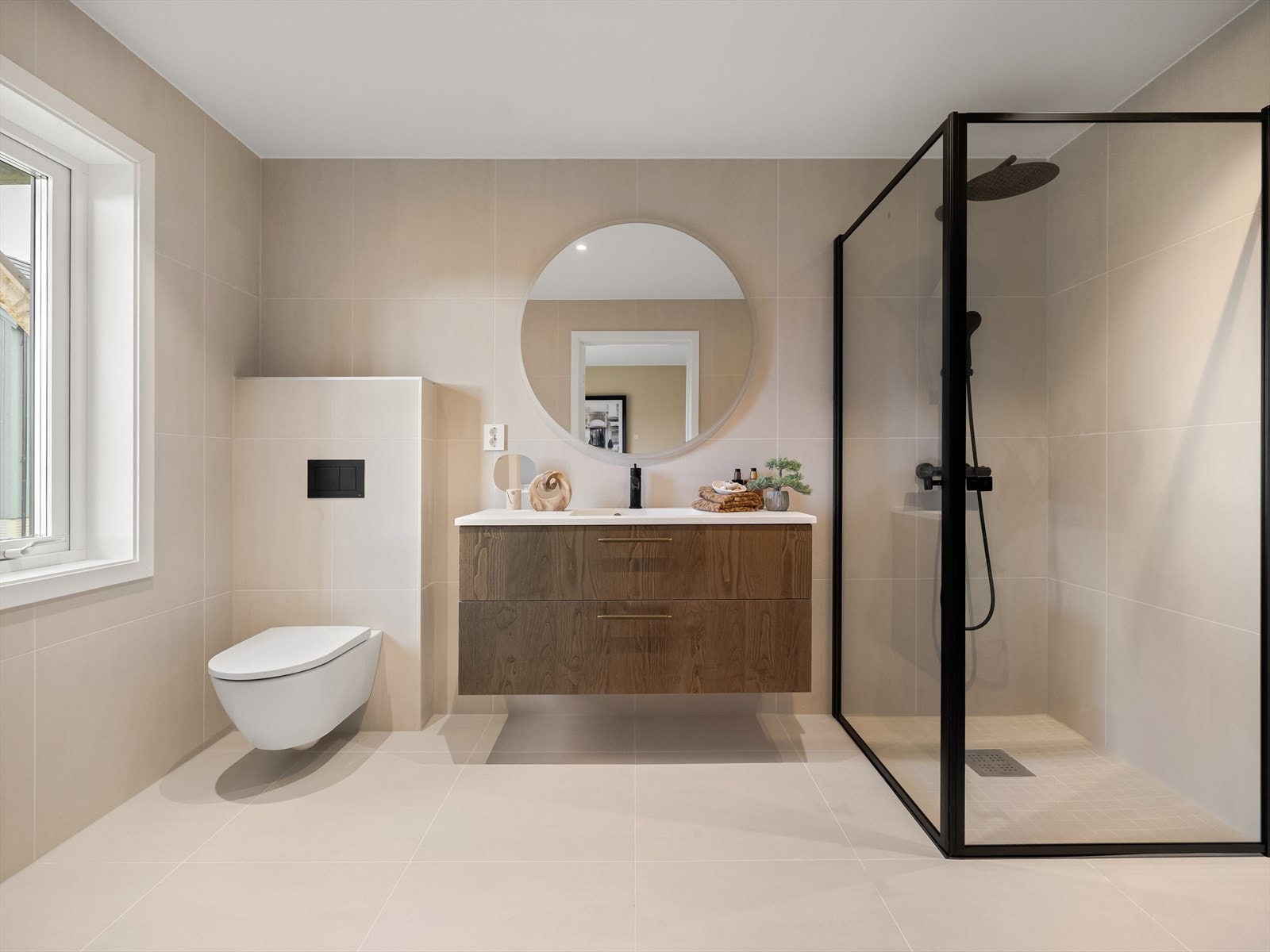 Badet i 1. etasje er utført i en moderne og tidløs stil med høy standard og gjennomtenkte detaljer. Praktisk servantseksjon i treverk gir både oppbevaringsplass og varme til rommene, mens stort speil og vindu bidrar til et luftig og lyst miljø. Galleribilde