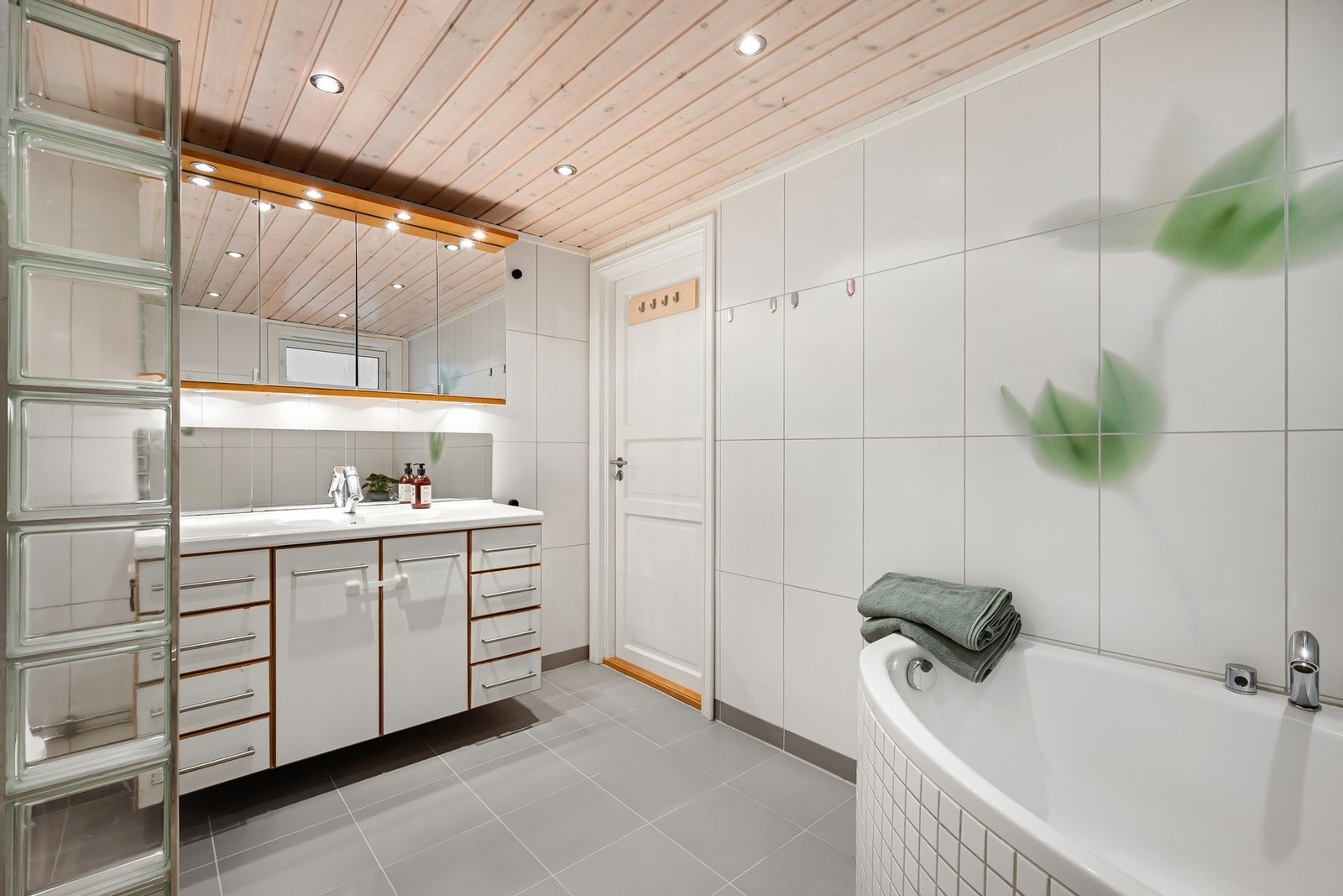 Badet har dusjkabinett, vegghengt toalett, innmurt badekar, servantskap med skuffer og speilskap med belysning. Fuktstyrt vifte sørger for god ventilasjon Galleribilde