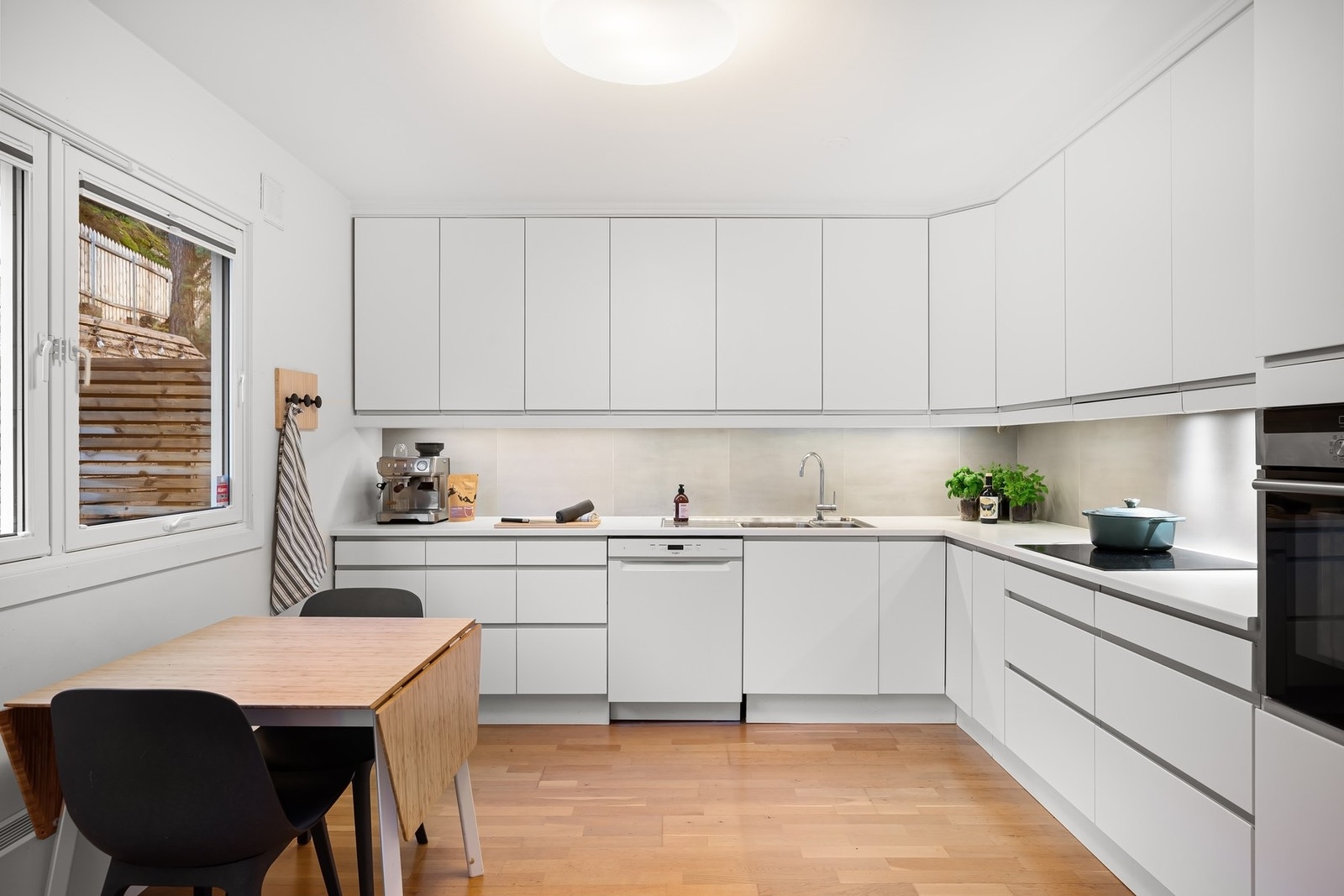 Delikat og tidløst kjøkken fra 2019 med hvite, glatte fronter og laminert benkeplate. Dobbel stålkum, underbelysning og fliser mellom benk og overskap gir et rent og stilfullt inntrykk Galleribilde