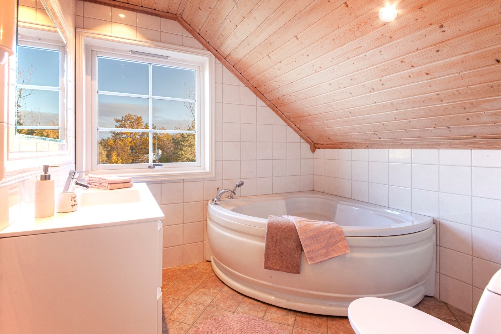 Badet i andre etasje har hjørnebadekar, gulvfestet toalett og hvit baderomsinnredning med skuffer. Galleribilde