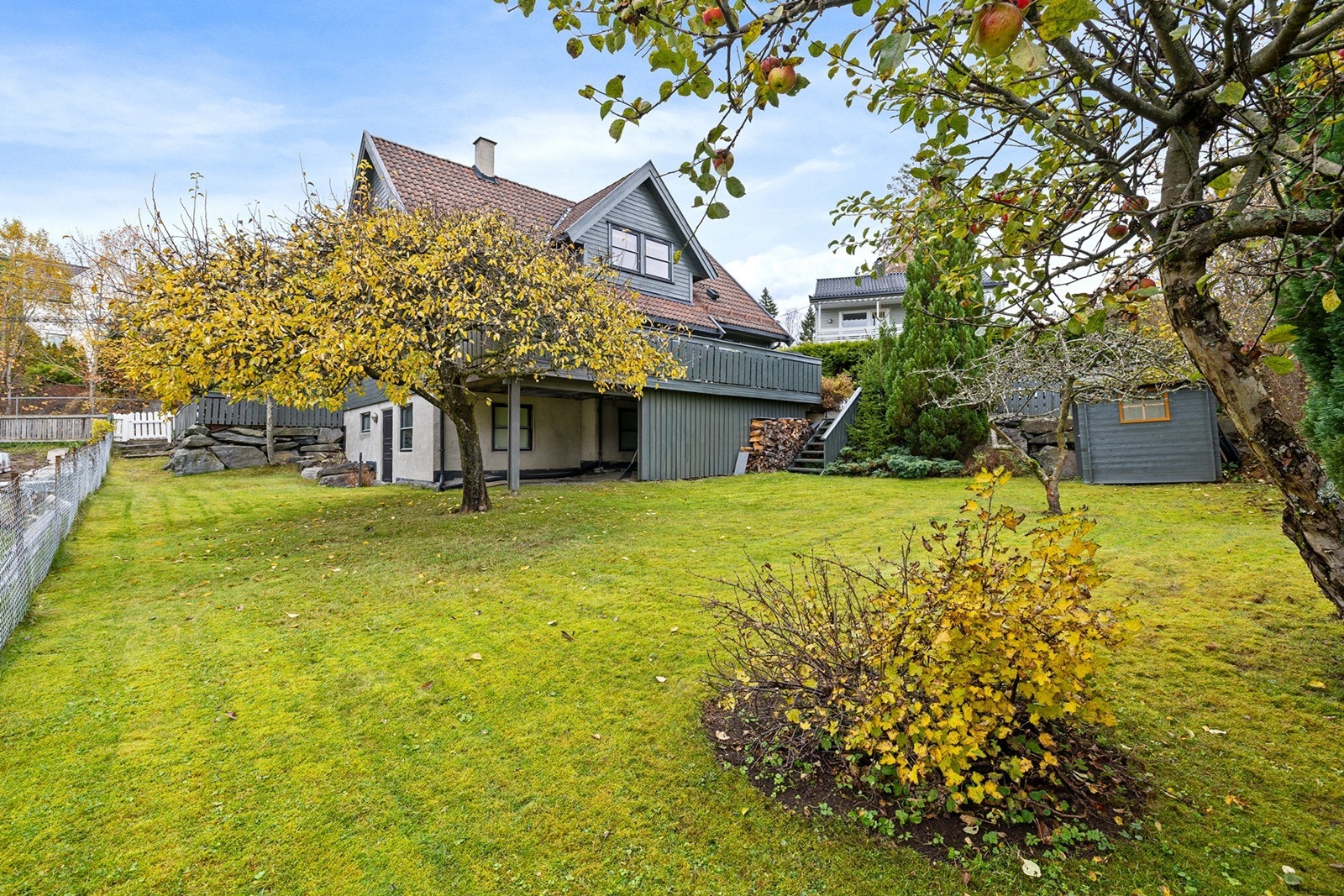 Tomten fremstår som velstelt og tilpasset terrengets naturlige høydeforskjeller, med plenarealer, prydbusker og beplantning som gir et frodig og innbydende preg. Galleribilde