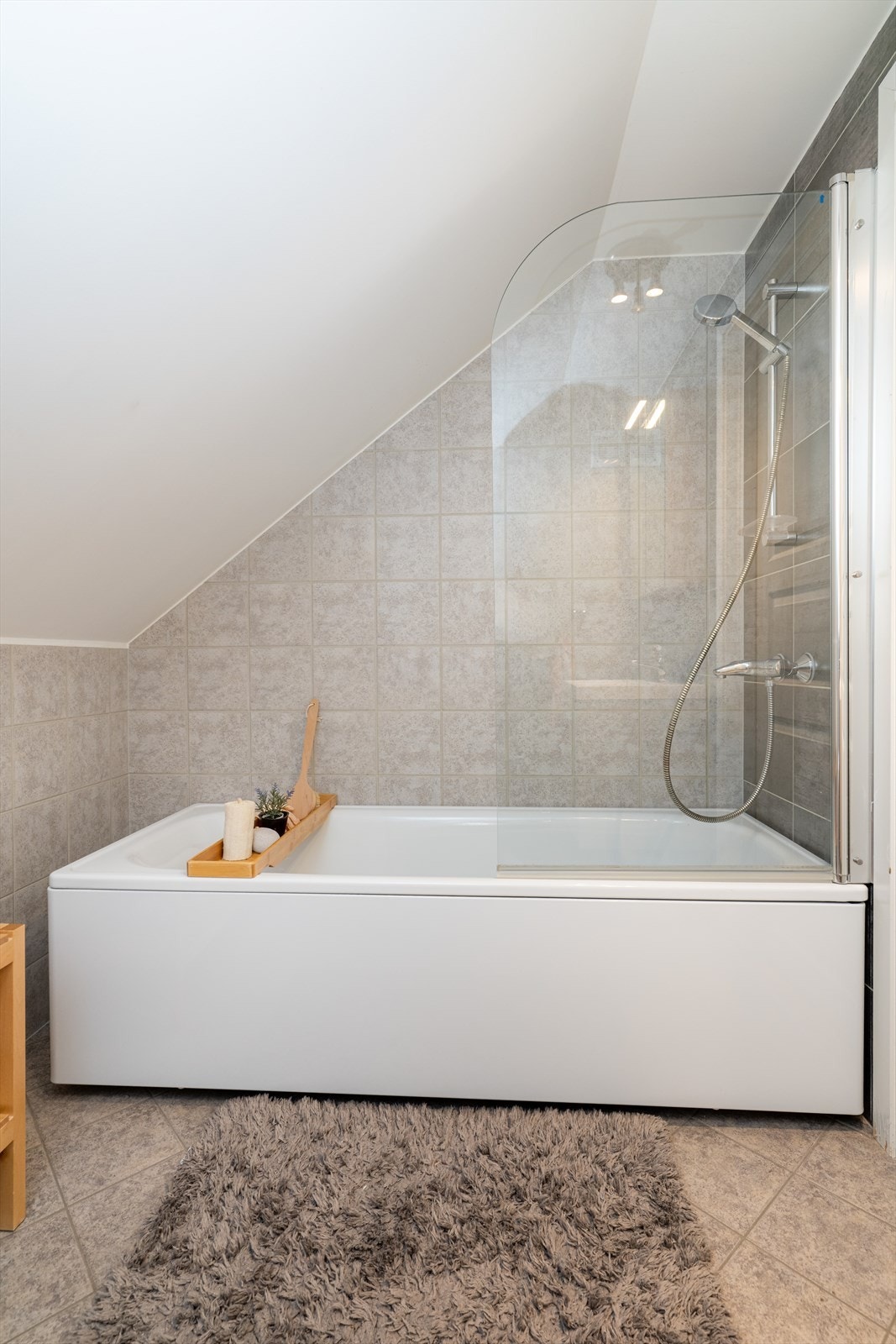 Badet er også innredet med badekar med dusjvegg og veggmontert toalett. Rommet er utstyrt med elektrisk vifte og tilluftspalte ved dør. Galleribilde