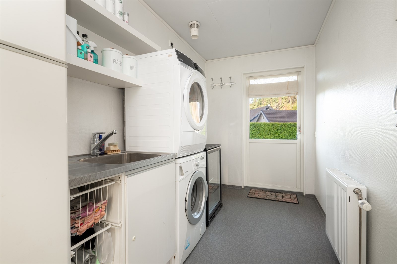 Boligen har et meget praktisk vaskerom av god størrelse, med utgangsdør mot hagen. Her har man et godt arbeidsrom med skap- og hylleplass, samt benk med nedfelt vaskekum. Galleribilde