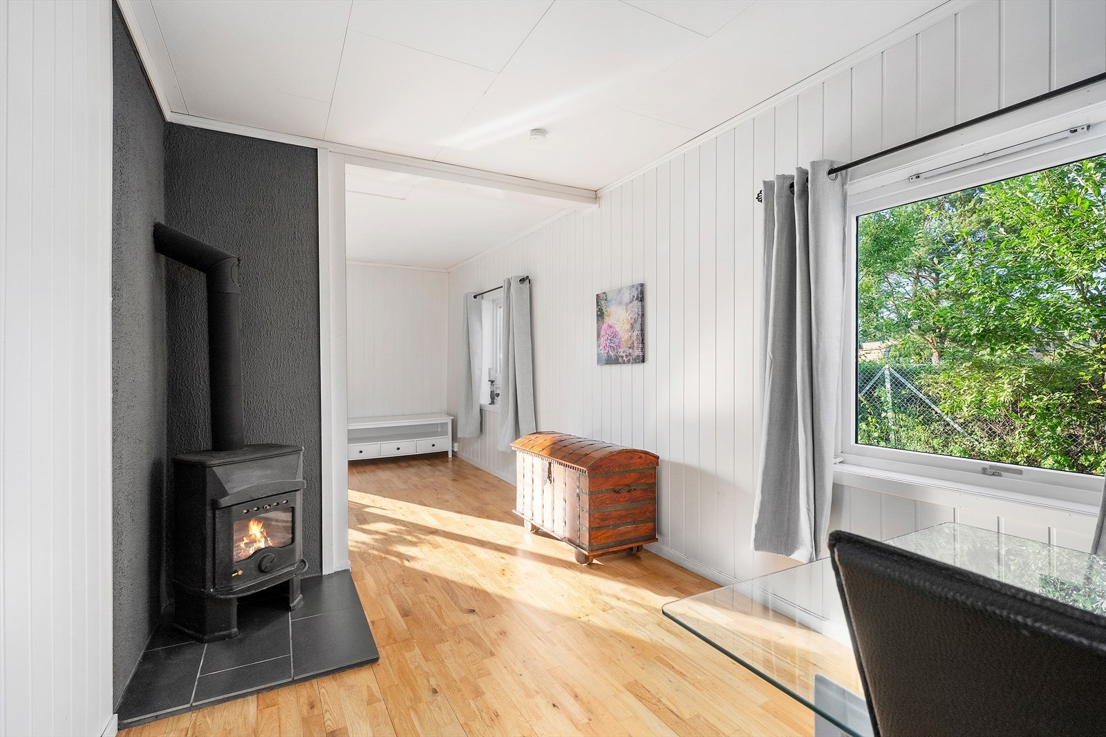 Spisetuen har vedovn og lyse tregulv. Mørk kontrastvegg og flislagt base rundt ovnen gir et moderne uttrykk. Galleribilde