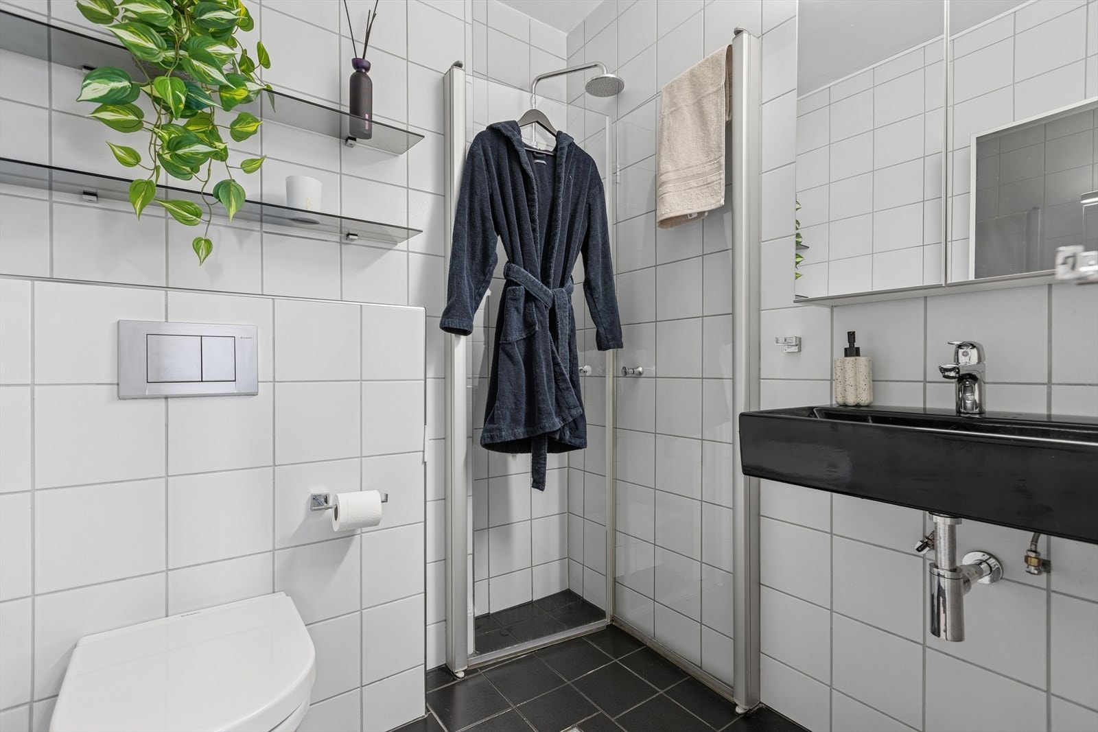 Baderommet er innredet med vegghengt servant, dusjhjørne med innfellbare dører, toalett og vegghengt speilskap. Galleribilde