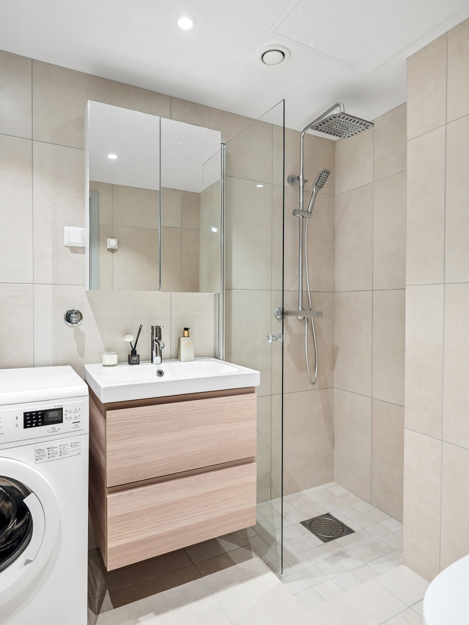 Rommet fremstår lyst og moderne, med servantinnredning, speilskap, dusjhjørne med nedsenk- og innfellbar glassdør, og gulvstående toalett. Galleribilde