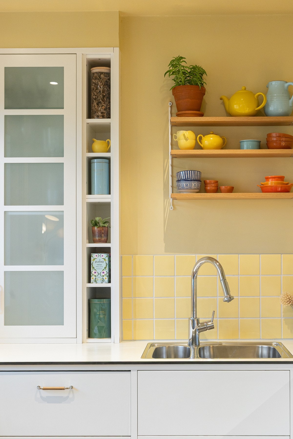 Mellom benkeplate og overskap er det lagt gule fliser som harmonerer fint med veggenes varme gulfarge og bidrar til et helhetlig og karakterfullt kjøkkenmiljø. Galleribilde