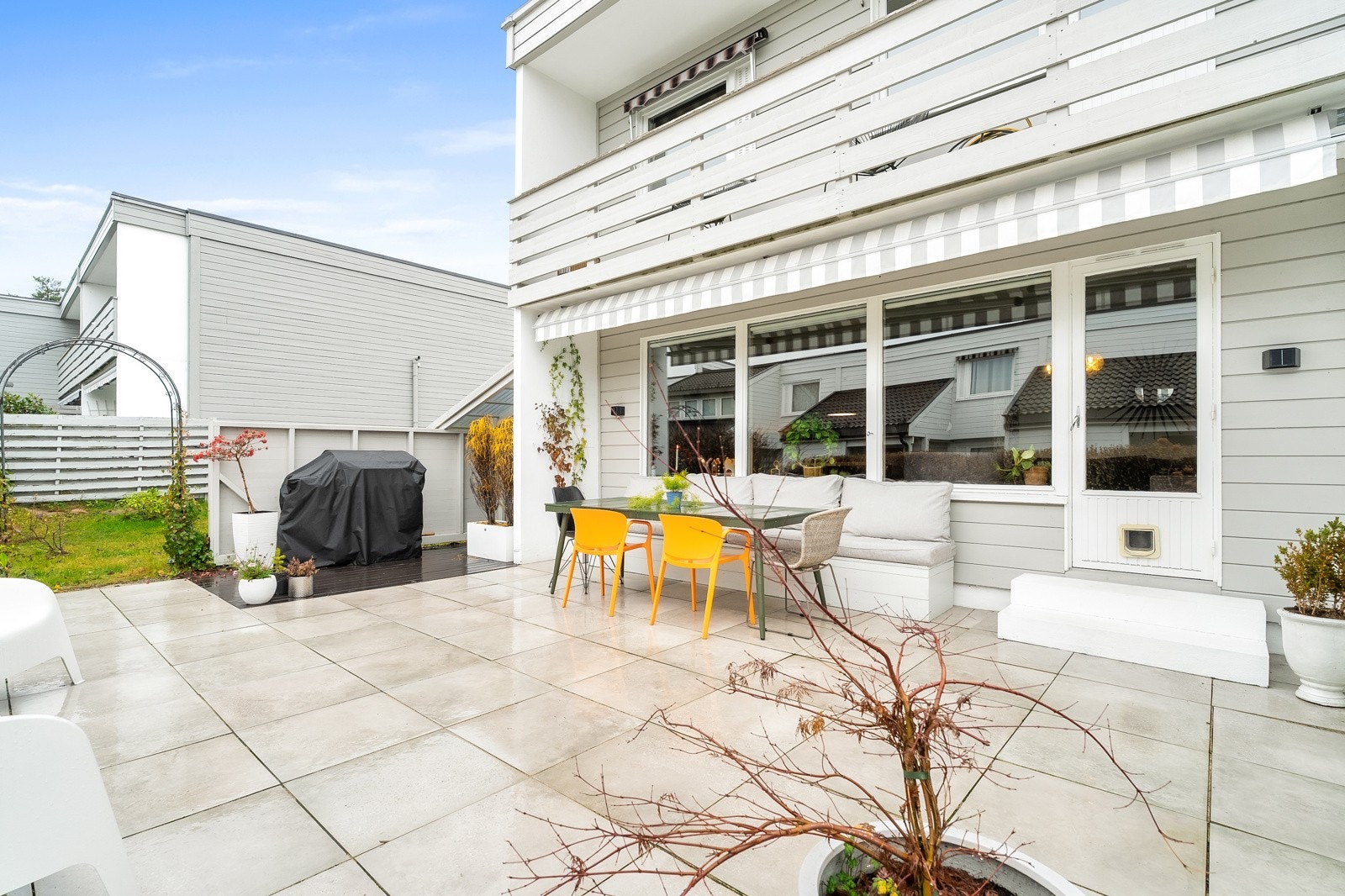 Vestvendt uteplass med fliser på dekket, markise og god plass til utemøblene. Galleribilde