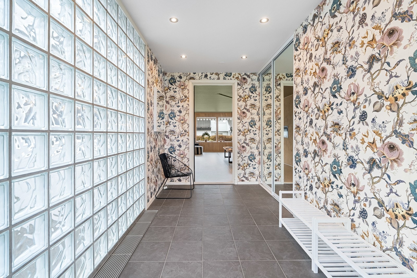 Romslig entré i 1. etasje med solide gulvfliser, downlightsbelysning og dekorativ tapetvegg kombinert med glassbyggerstein. Galleribilde