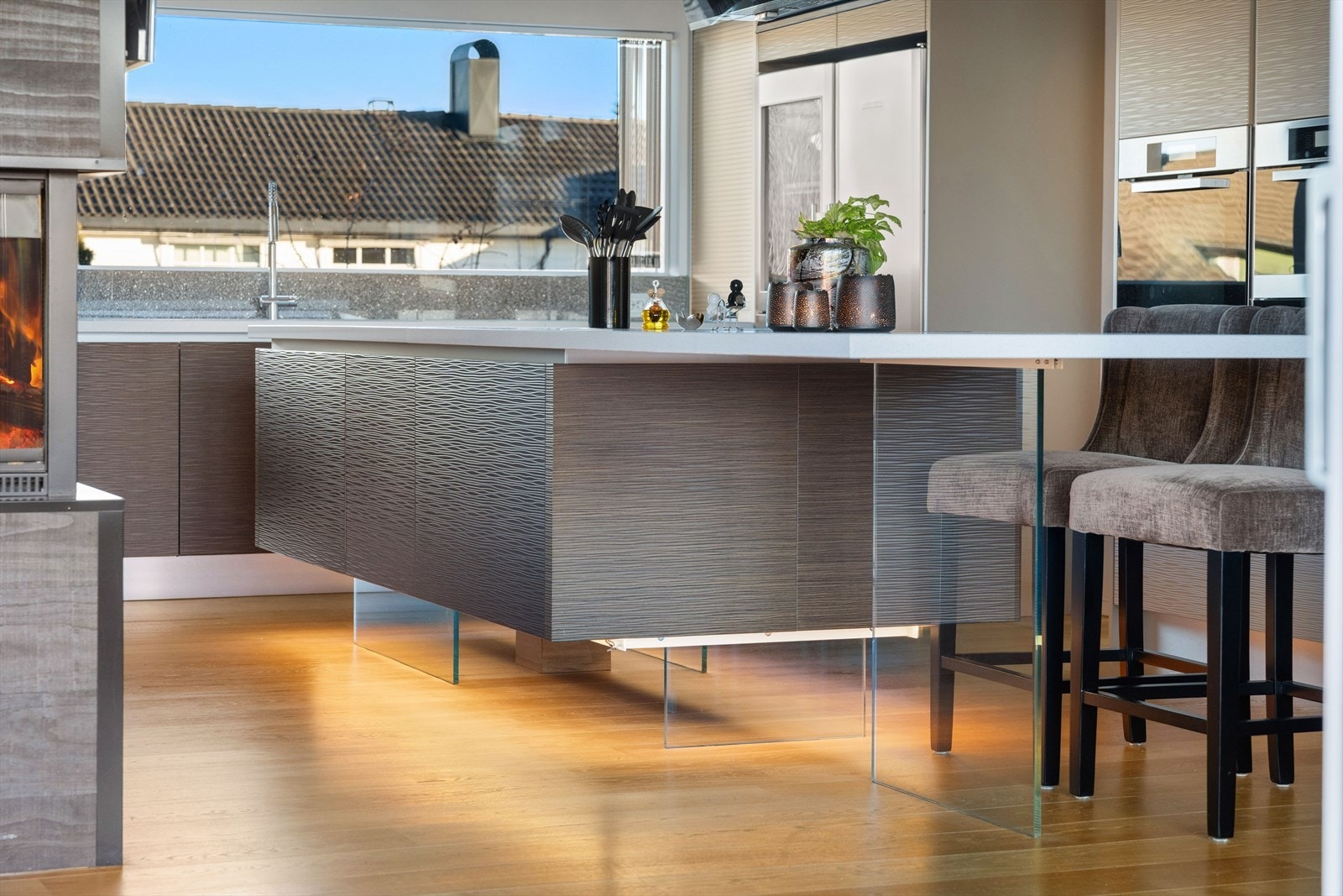 Kjøkkenøyen står på en smart glassokkel, det ser ut til at den svever i luften. Over kjøkkenbenken er det rikelig med naturlig lys fra det store vinduet over kjøkkenbenken. Galleribilde