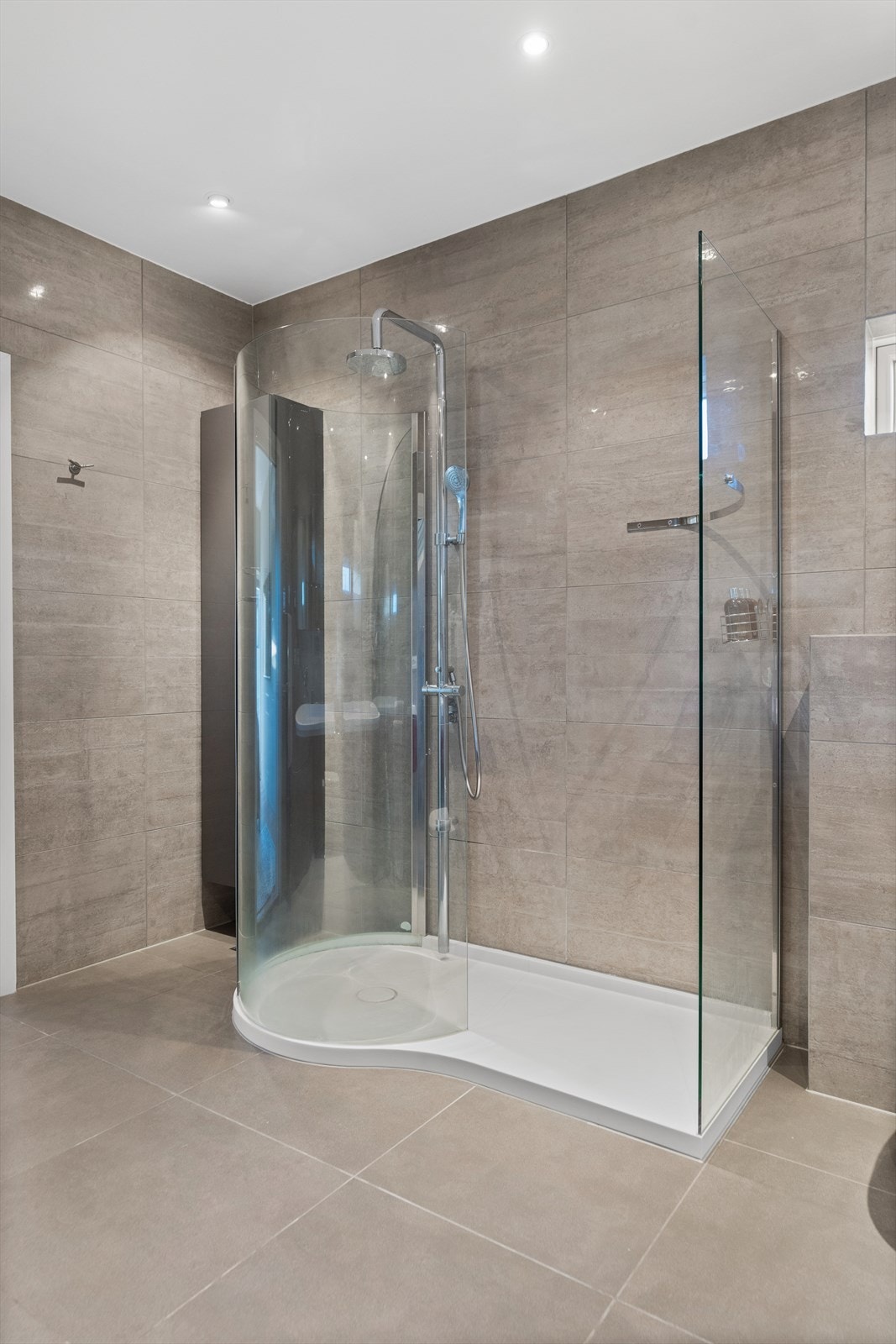 Videre er rommet utstyrt med vegghengt toalett og dusjkabin med buet glassvegg på formstøptdusjbunn, i samme fasong som baderomsinnredningen. Galleribilde