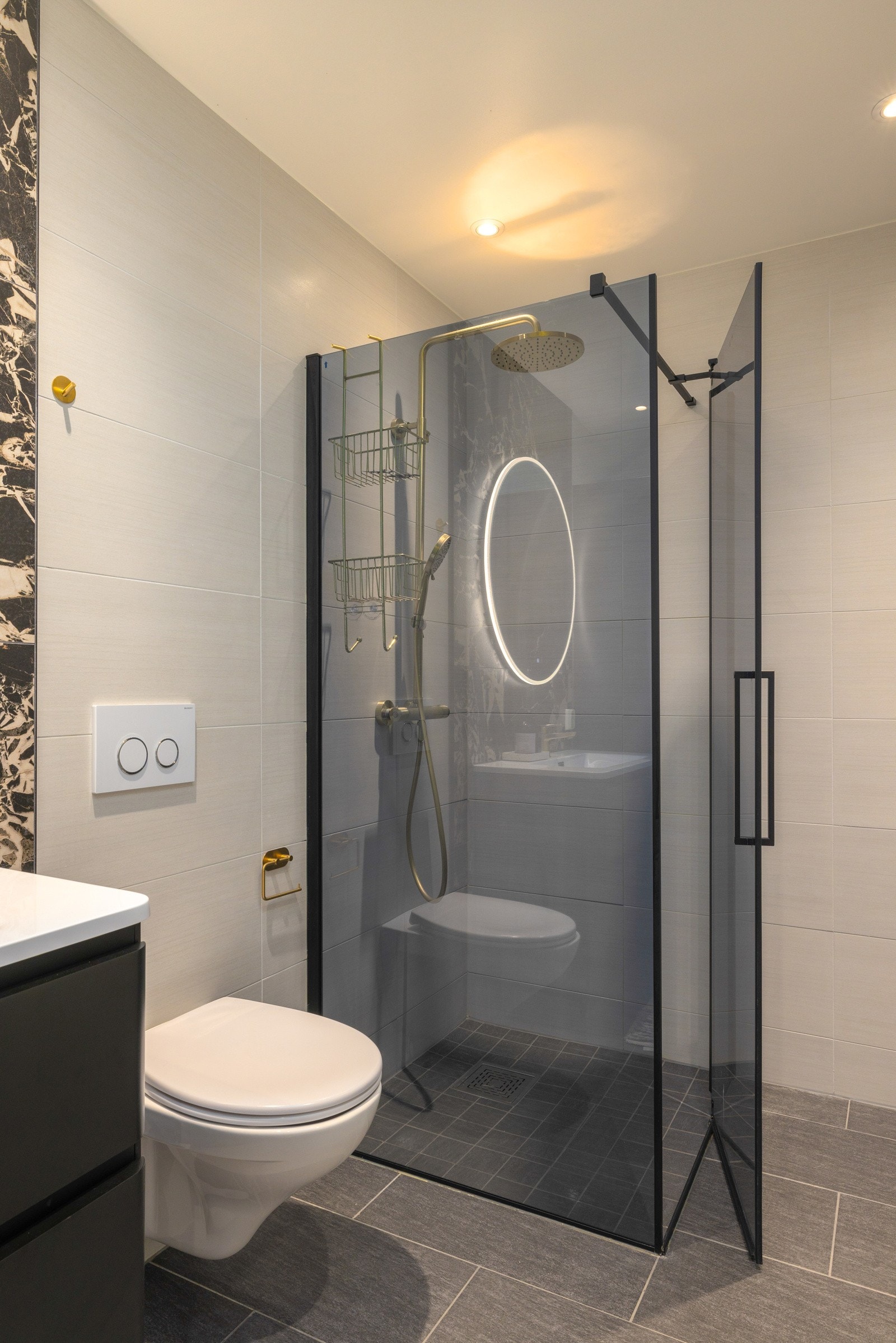 Vegghengt toalett og stilfull dusjløsning med glassvegger og sorte detaljer. Galleribilde