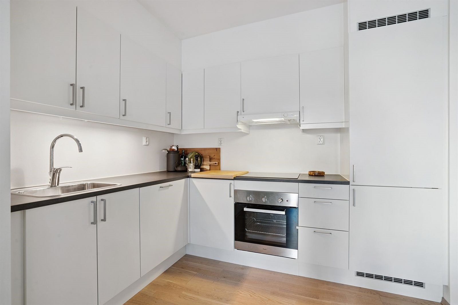 Lyst og behagelig kjøkken med moderne og hvite, glatte fronter med integrerte hvitevarer. Galleribilde