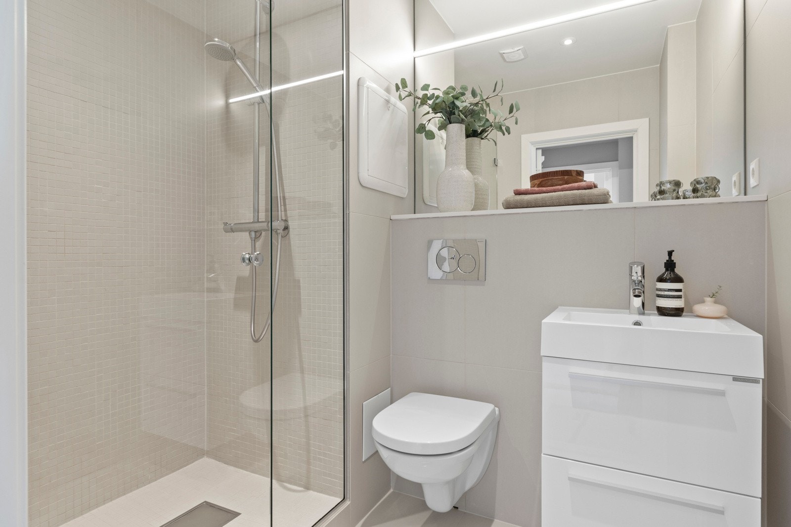 Innredet med vegghengt wc, servant med skuffer under, veggspeil og dusjnisje. Galleribilde