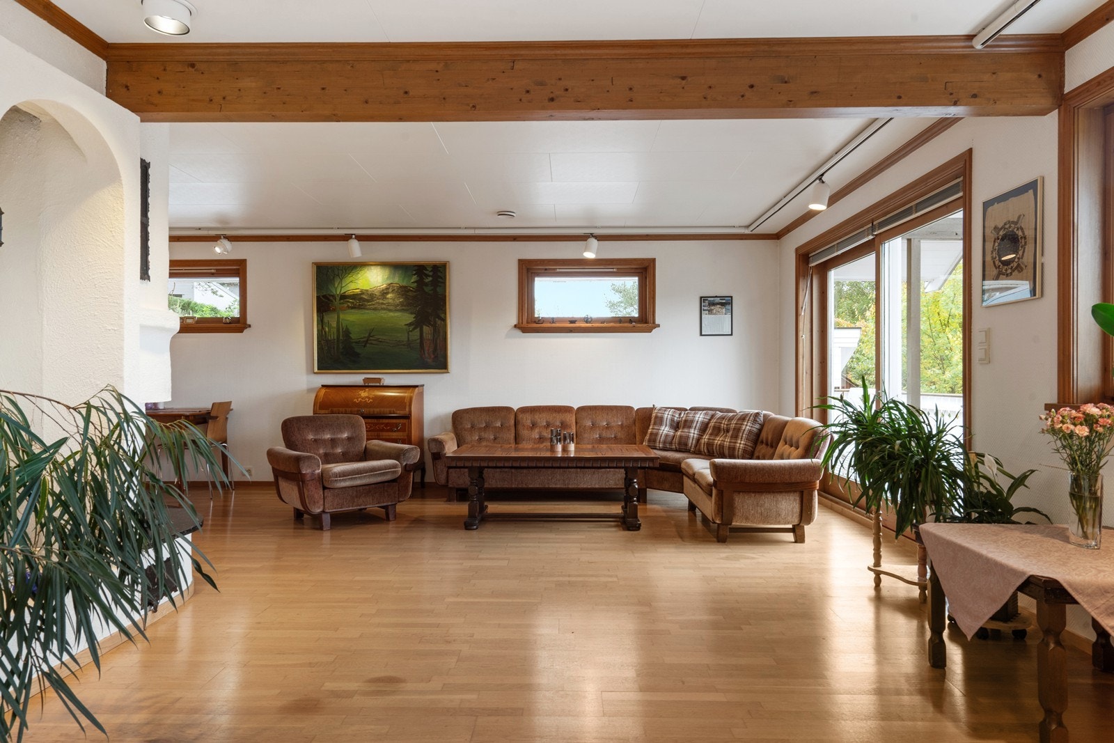 Stor og lys stue i vinkel med plassmurt vedovn og skyvedør i glass ut mot veranda Galleribilde