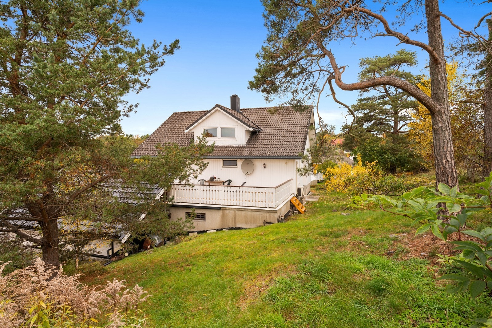På baksiden av boligen har du noe gressplen og ellers naturtomt med busker, trær og fjell i dagen Galleribilde
