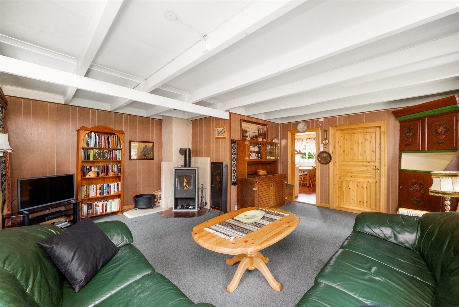 Stuen er et trivelig rom med panel på vegger og synlige trebjelker i hvitmalt himling. Galleribilde