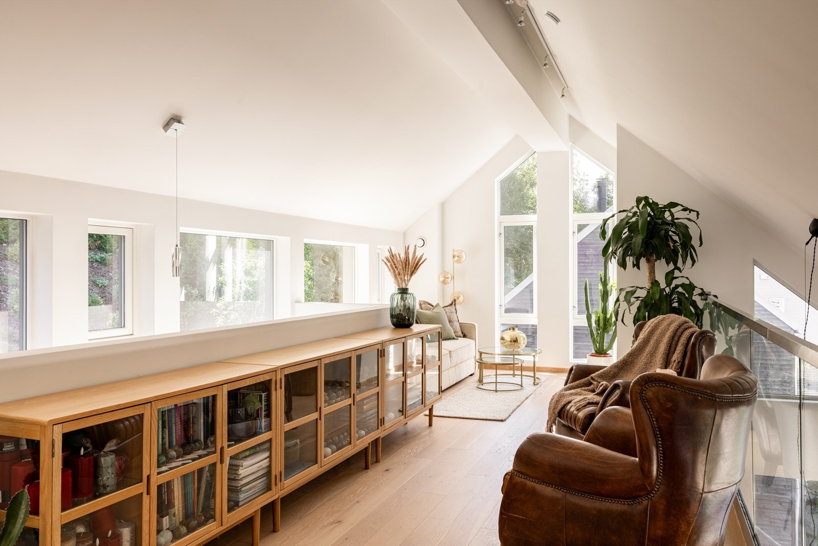 Åpen loftstue med stilrent glassrekkverk fra PKS - et galleri mot stuen. Gulvet i rommet er i enstavs parkett og overflatene er lysmalte med listefri overgang mellom himling, vinduer og vegger. Galleribilde