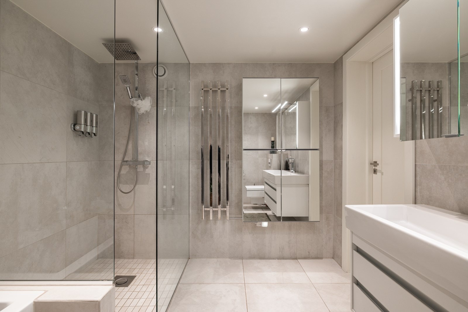 Innredningen består av en heldekkende servant på hvit skuffeseksjon, speilskap med belysning over servanten, et firedørs veggskap med speil samt veggmontert toalett og en håndkletørker. Galleribilde