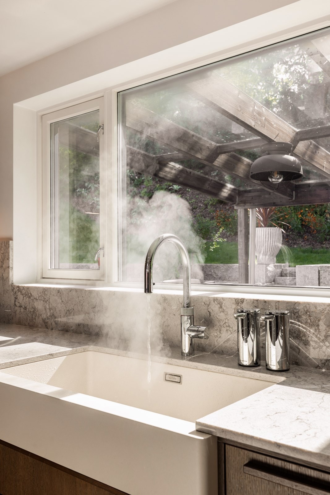 Benkeplaten er i tynn, marmorert stein med matchende backsplash. Vaskekummen er i porselen med Quooker-kran med både kullsyrevann og kokende vann. Galleribilde